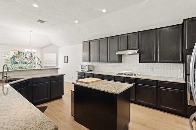 kitchen with light wood-style flooring, vaulted ceiling, a sink, gas cooktop, and under cabinet range hood