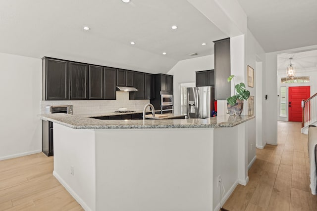 kitchen featuring appliances with stainless steel finishes, backsplash, light stone counters, and light wood-style floors