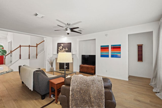 living area with visible vents, light wood-style flooring, ceiling fan, baseboards, and stairs