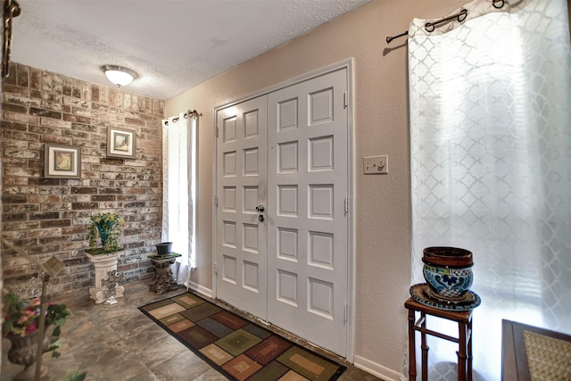 foyer with a textured ceiling, a textured wall, and brick wall