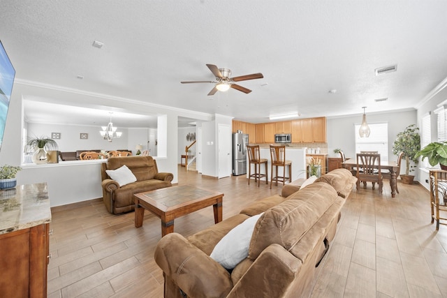 living room with visible vents, ornamental molding, a textured ceiling, light wood-style floors, and ceiling fan with notable chandelier