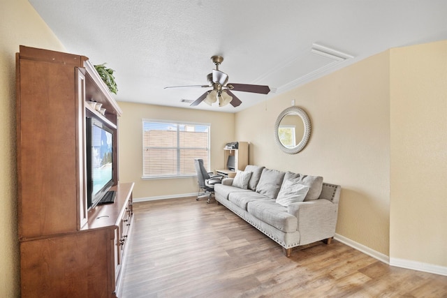 living room with a textured ceiling, light wood finished floors, a ceiling fan, and baseboards