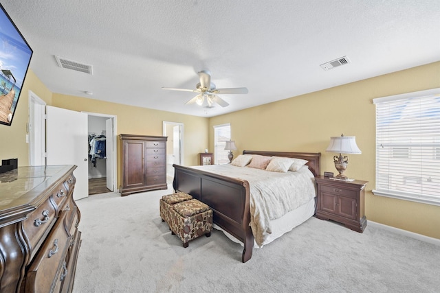 bedroom featuring light colored carpet, visible vents, a spacious closet, and a textured ceiling