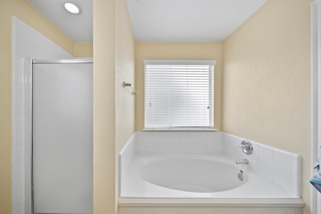 bathroom featuring a textured wall, a stall shower, and a bath