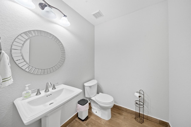 bathroom with visible vents, toilet, a sink, wood finished floors, and baseboards