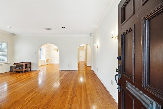 empty room with ornamental molding, arched walkways, visible vents, and light wood finished floors