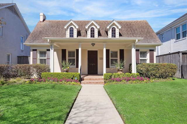 new england style home featuring a shingled roof, a front yard, covered porch, and fence