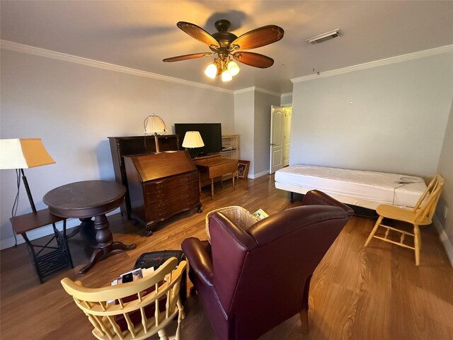 living room featuring wood finished floors, visible vents, baseboards, a ceiling fan, and ornamental molding