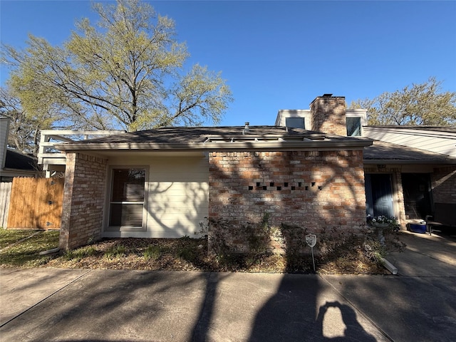 view of side of home featuring brick siding, fence, and a chimney