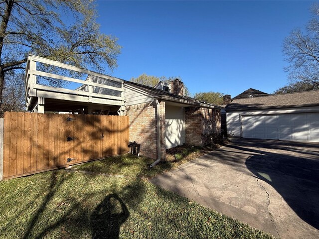 view of property exterior featuring a garage, concrete driveway, a chimney, fence, and brick siding