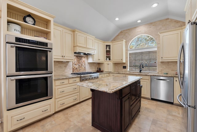 kitchen with a sink, cream cabinets, appliances with stainless steel finishes, lofted ceiling, and light stone countertops