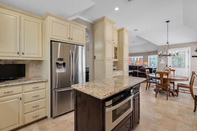 kitchen featuring cream cabinetry, stainless steel appliances, open floor plan, and decorative backsplash