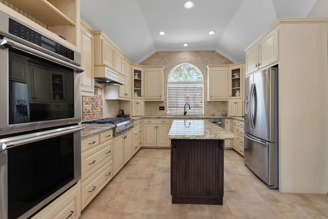 kitchen with light stone countertops, cream cabinets, appliances with stainless steel finishes, and vaulted ceiling