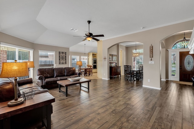 living room with visible vents, dark wood-type flooring, ornamental molding, ceiling fan with notable chandelier, and arched walkways