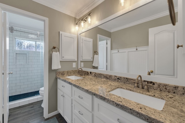 bathroom featuring a sink, tiled shower, toilet, and crown molding