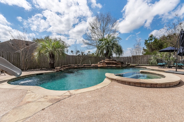 view of swimming pool with a patio area, a pool with connected hot tub, a water slide, and a fenced backyard