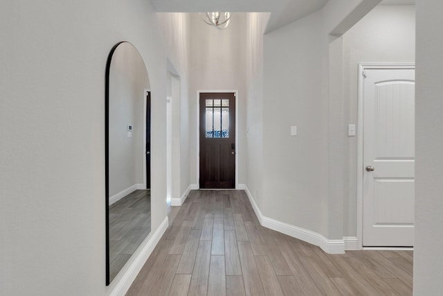 foyer entrance featuring light wood-style floors, baseboards, arched walkways, and a chandelier