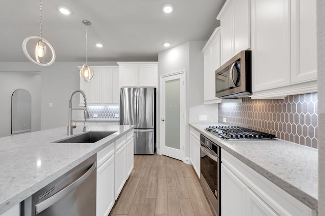 kitchen with a sink, white cabinetry, appliances with stainless steel finishes, decorative backsplash, and light wood finished floors