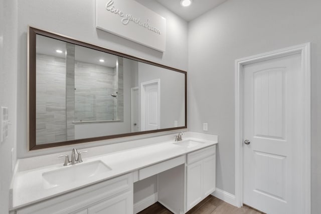 bathroom with a tile shower, double vanity, wood finished floors, and a sink