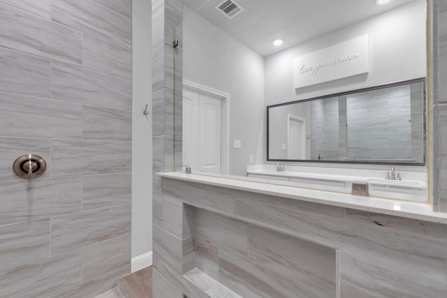 bathroom featuring visible vents, a tile shower, and vanity