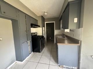 kitchen featuring light tile patterned floors, range with gas cooktop, range hood, gray cabinets, and a sink