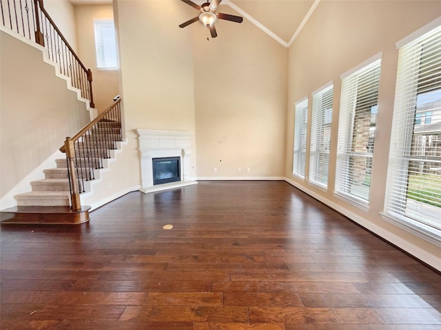 unfurnished living room featuring crown molding, a towering ceiling, dark wood-type flooring, a glass covered fireplace, and baseboards