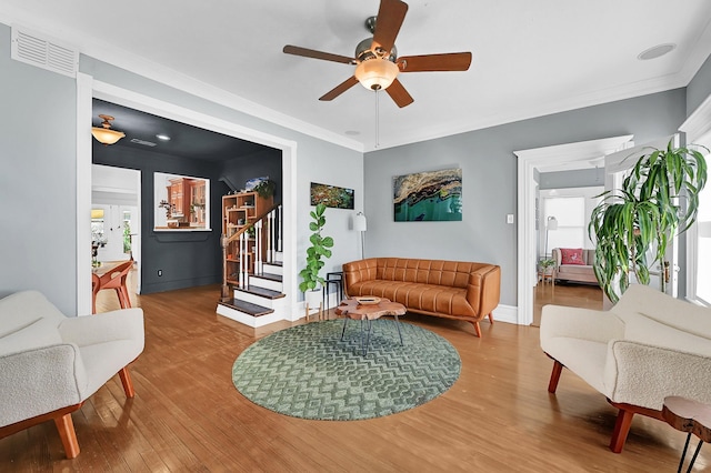 living area featuring crown molding, visible vents, a ceiling fan, wood finished floors, and stairs