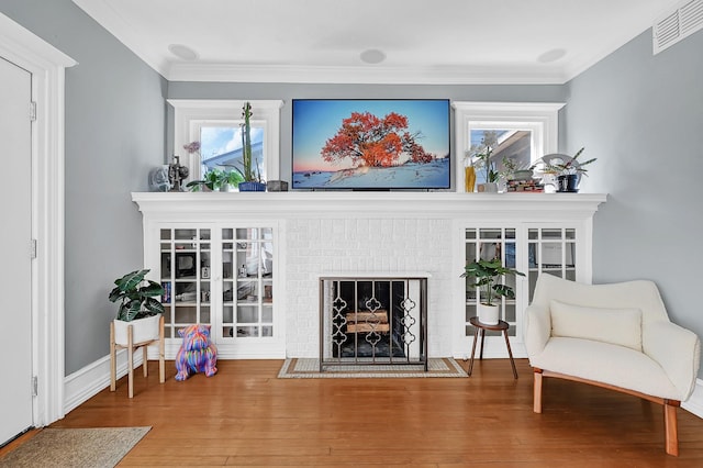 sitting room with a fireplace, wood finished floors, visible vents, and crown molding