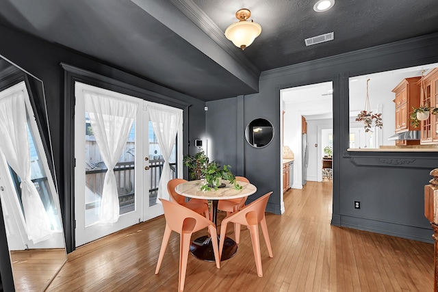 dining area with a healthy amount of sunlight, light wood-type flooring, visible vents, and crown molding