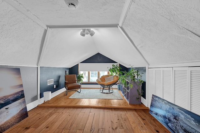 sitting room with baseboards, visible vents, lofted ceiling, hardwood / wood-style flooring, and a textured ceiling