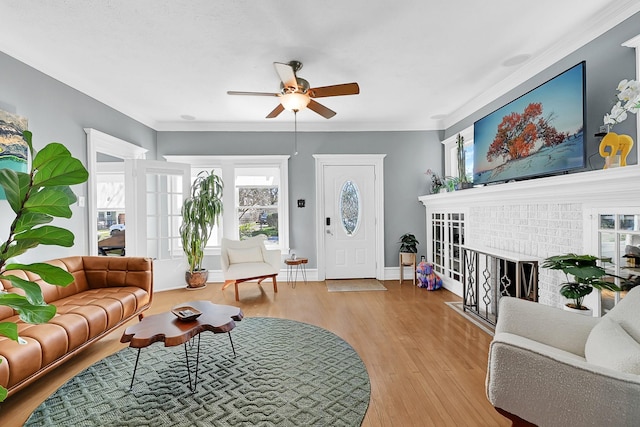 living area featuring a ceiling fan, ornamental molding, a brick fireplace, wood finished floors, and baseboards