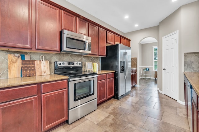 kitchen featuring decorative backsplash, arched walkways, appliances with stainless steel finishes, and reddish brown cabinets