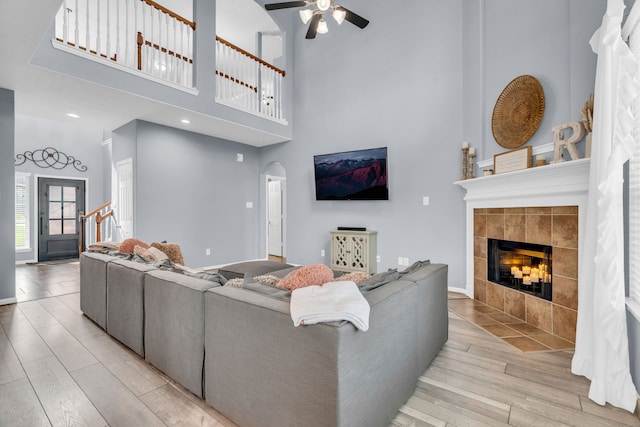 living area featuring arched walkways, light wood-style floors, ceiling fan, stairs, and a tile fireplace