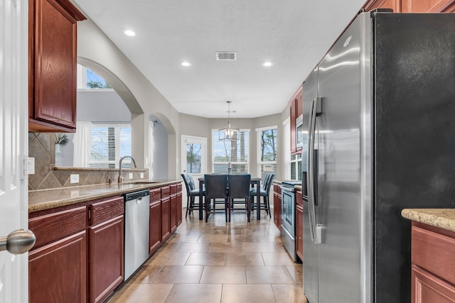 kitchen featuring light tile patterned floors, decorative backsplash, hanging light fixtures, stainless steel appliances, and a sink