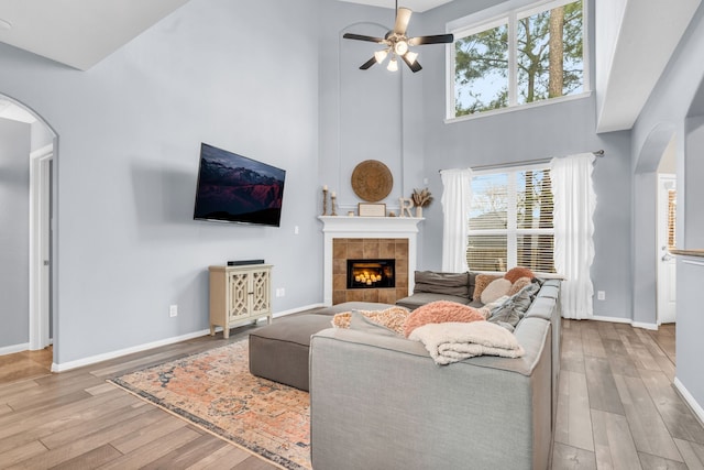 living area with a ceiling fan, wood finished floors, baseboards, arched walkways, and a tiled fireplace