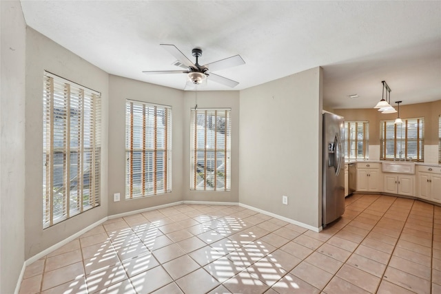 unfurnished dining area featuring a sink, baseboards, a ceiling fan, and light tile patterned flooring