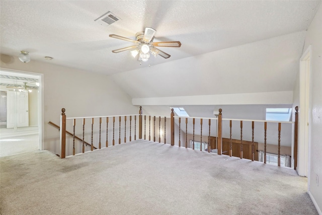 additional living space featuring ceiling fan, a textured ceiling, carpet flooring, visible vents, and vaulted ceiling