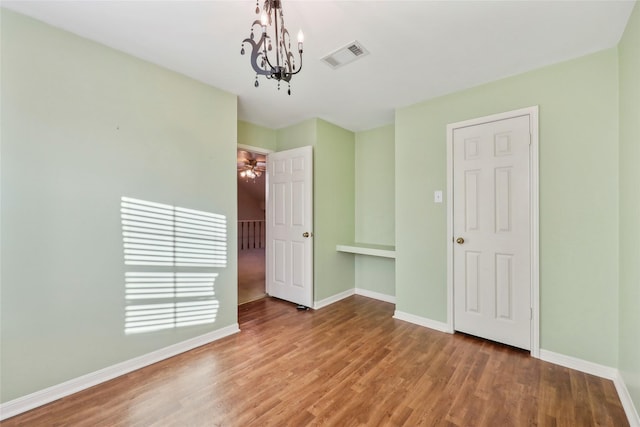 unfurnished bedroom featuring an inviting chandelier, visible vents, baseboards, and wood finished floors