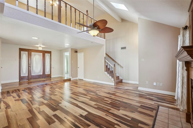 unfurnished living room featuring a stone fireplace, a skylight, wood finished floors, visible vents, and stairway