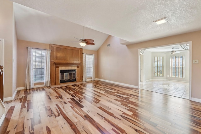 unfurnished living room featuring lofted ceiling, light wood finished floors, a textured ceiling, and a fireplace with flush hearth