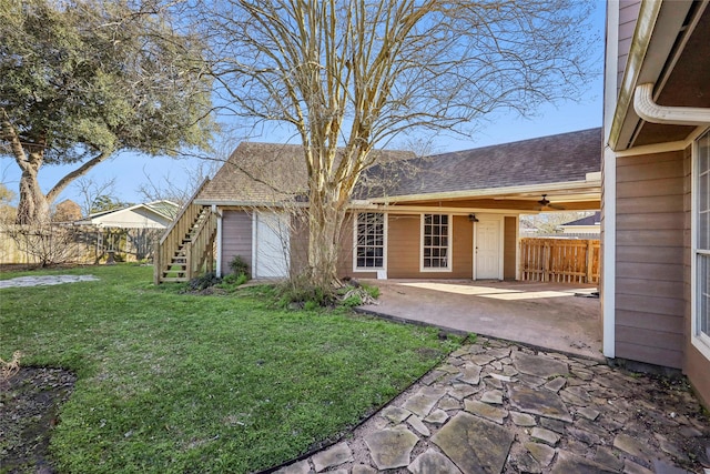 rear view of property with a lawn, a patio, stairway, roof with shingles, and fence