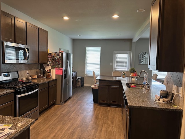 kitchen featuring dark stone counters, stainless steel appliances, dark brown cabinets, light wood-style floors, and a sink