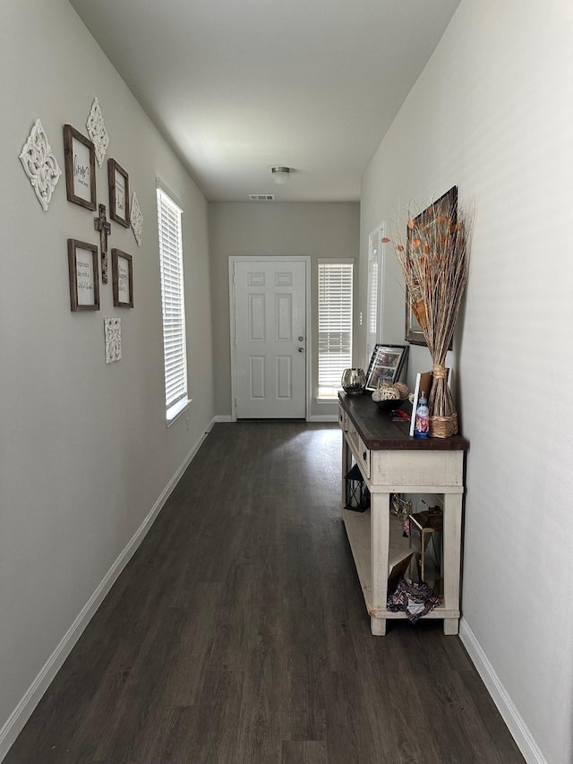 hall featuring dark wood finished floors, visible vents, and baseboards