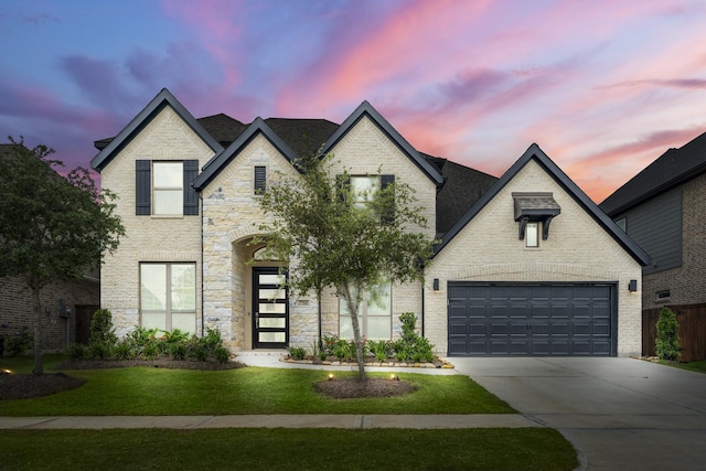 french provincial home with concrete driveway, a yard, and brick siding