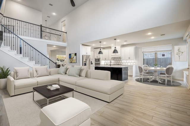 living area featuring recessed lighting, light wood-style flooring, stairway, a towering ceiling, and baseboards