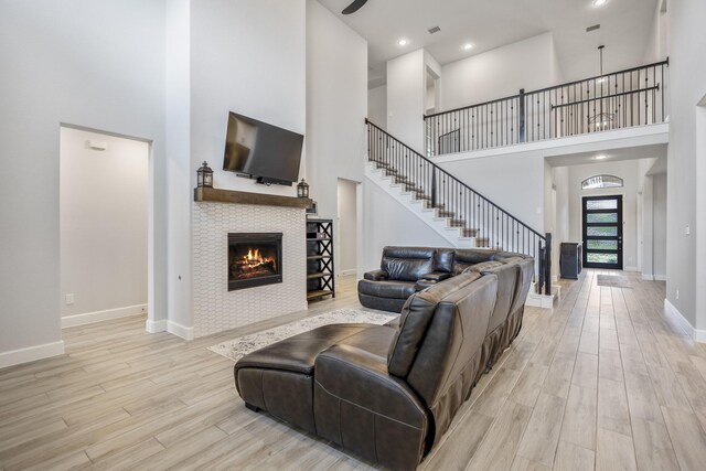 living room with stairway, a high ceiling, a tiled fireplace, light wood-type flooring, and baseboards