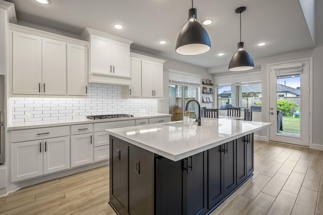 kitchen featuring stainless steel gas cooktop, a sink, white cabinetry, light countertops, and decorative backsplash