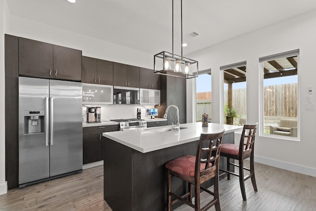 kitchen with a sink, light countertops, appliances with stainless steel finishes, decorative backsplash, and a kitchen bar