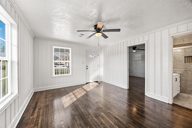 unfurnished living room featuring dark wood-style flooring, visible vents, ornamental molding, a textured ceiling, and baseboards