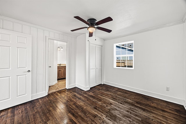 unfurnished bedroom featuring a closet, baseboards, dark wood finished floors, and crown molding